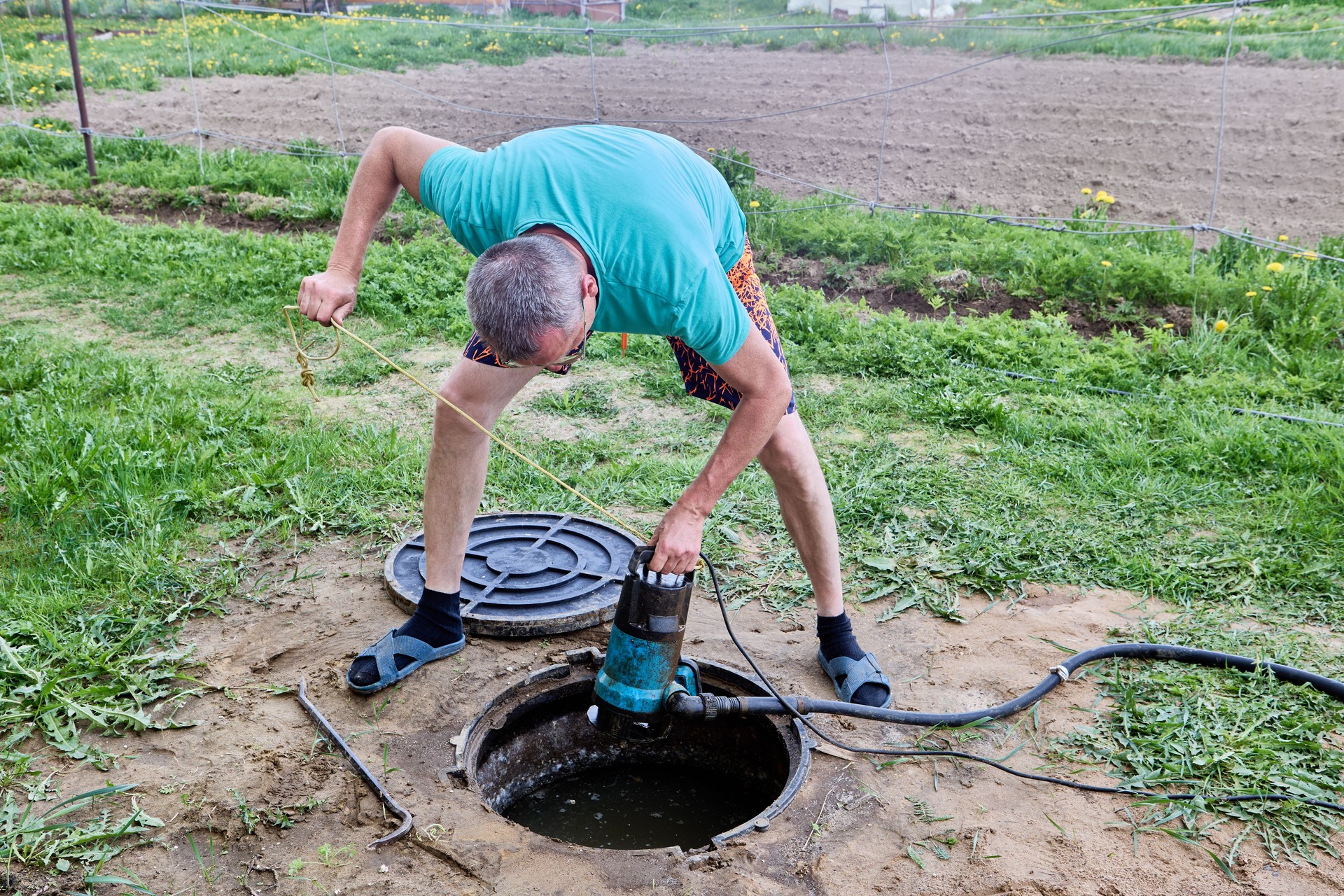 Man lowers high pressure submersible drainage pump into septic tank to pump sewage and dispose of it.