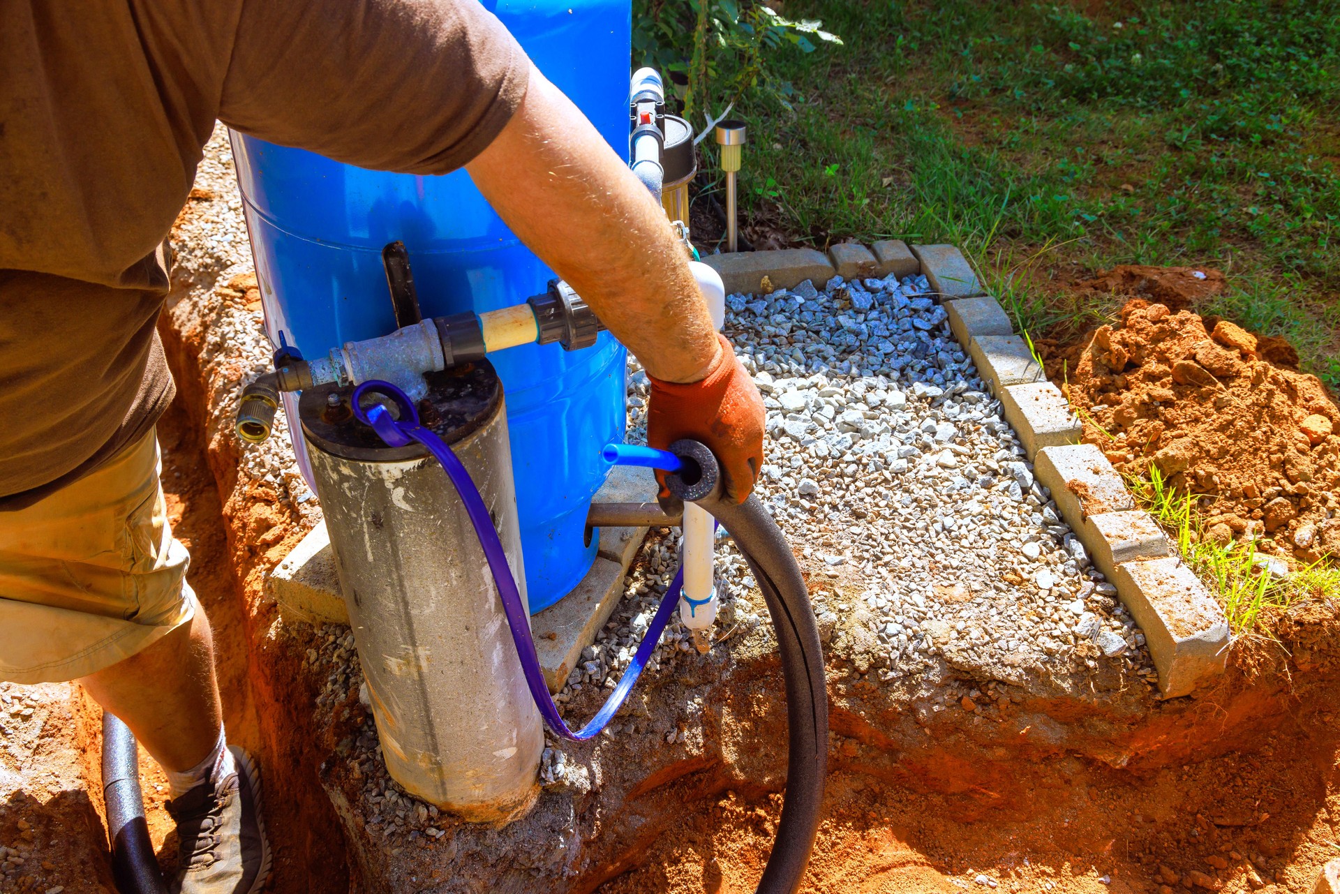 Worker installing water pump system in residential yard during sunny afternoon